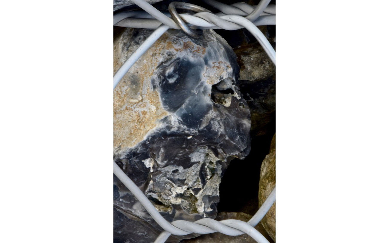 Le silex éclaté dessine deux yeux blancs dans des orbites bleues sombre. Le bouche a un aspect "gueule cassée" qui fait penser au masque de Dark Wador. L'enfer du gabion 13-Le côté obscur de la force-Les pierres du chemin-Photo J Lamy 2019.