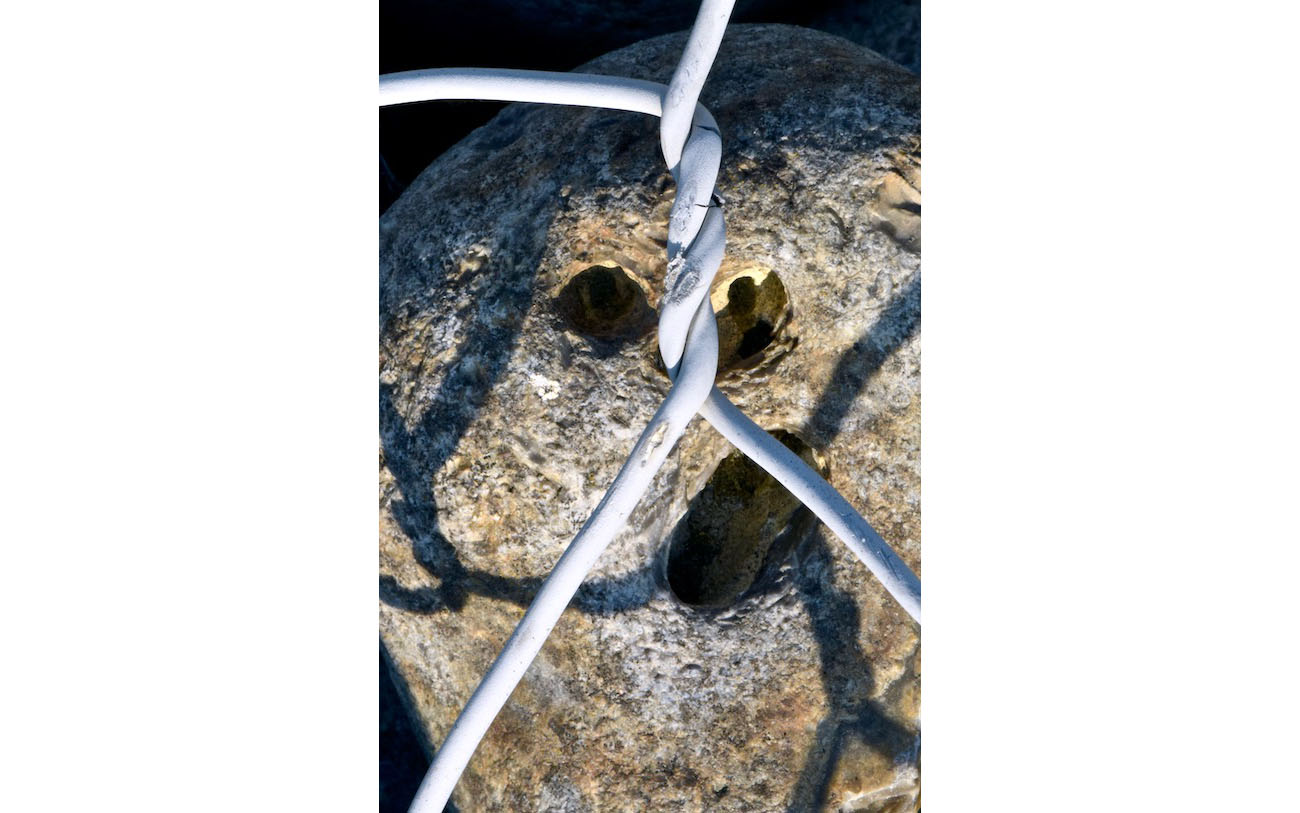 L'enfer du gabion 8- Le bourreau dans la pupille- Photo J Lamy-2019- S portfolio. L'ombre du grillade sur le visage accroche le coin de la bouche. La menace est redoublée par l'ombre d'une sihlouette, tel un reflet dans la pupille de pierre vide.